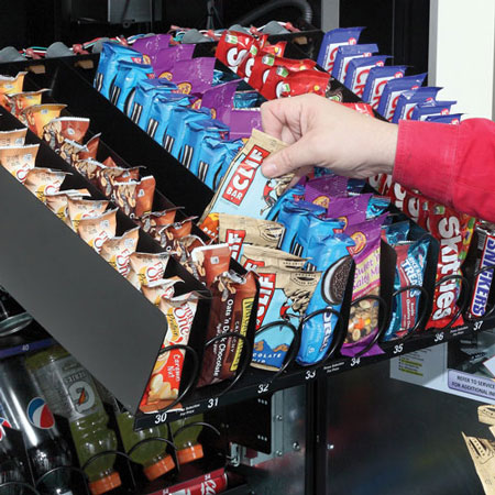 Vending operator stocking snack vending machine with popular snacks for customers.